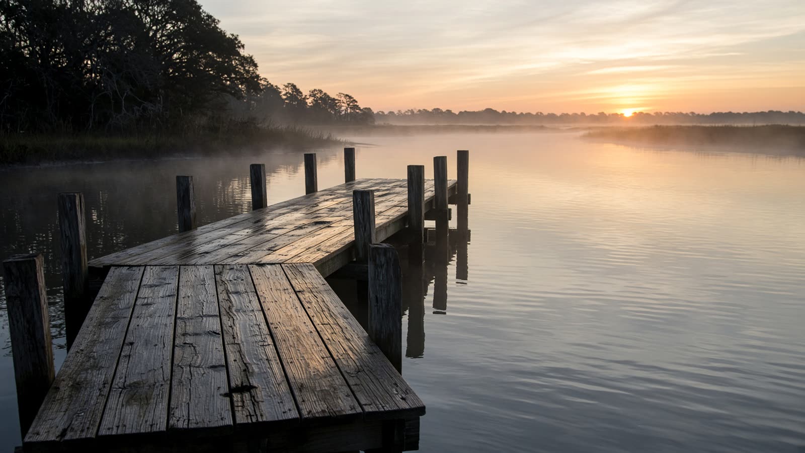 A wooden dock reaching into still water on the Chesapeake Bay at sunrise